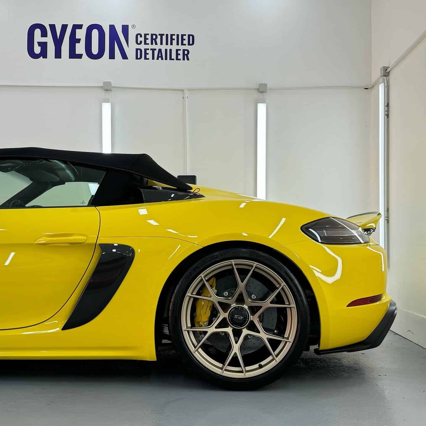 Side profile of a yellow Porsche 718 Spyder RS, with a Gyeon Certified Detailer logo in the background